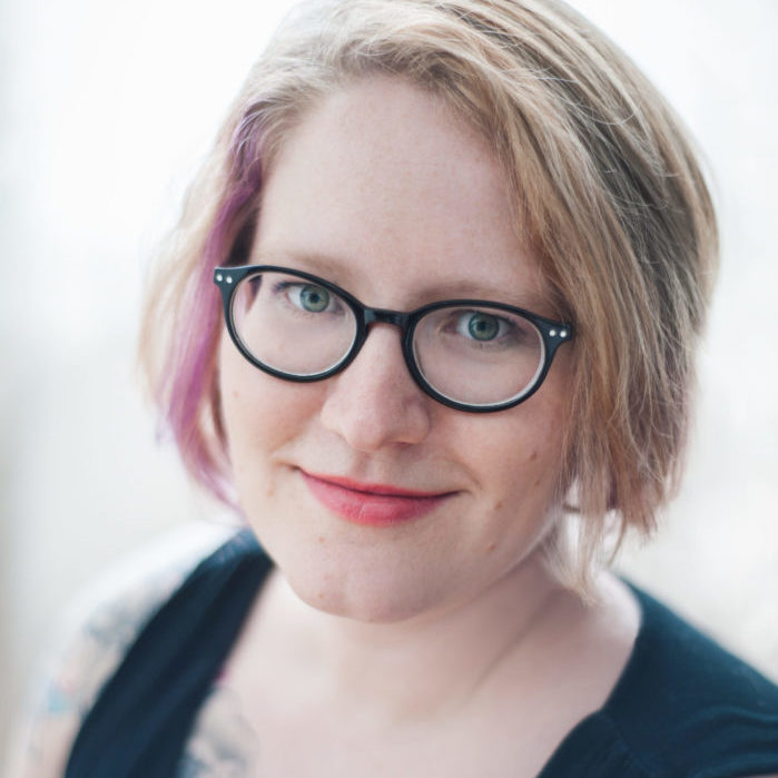 Sarah Harvey headshot: woman with glasses and purple streak in her blond hair looking into camera